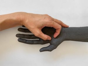 Alexandra Ridel's hand resting in the hand of a dark stoneware sculpture