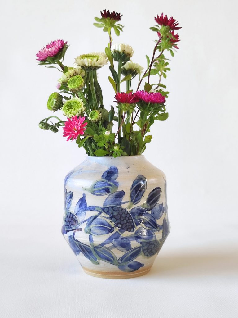 Decorative vase with cobalt blue botanical decoration, holding a bouquet of daisies, by Alexandra Ridel