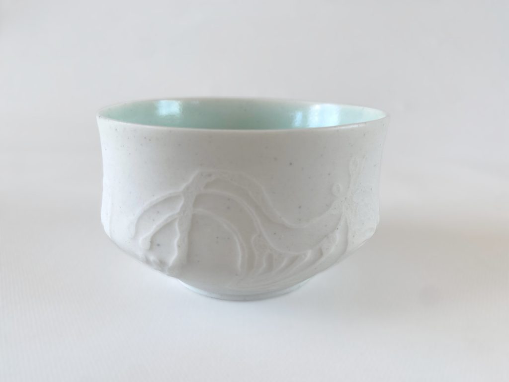 White porcelain cup with carved exterior decoration and light blue glaze, by Alexandra Ridel
